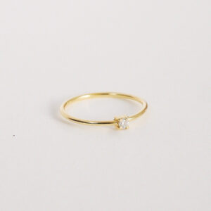 Anel solitário em ouro amarelo 18k com diamante em lapidação brilhante sobre fundo branco.