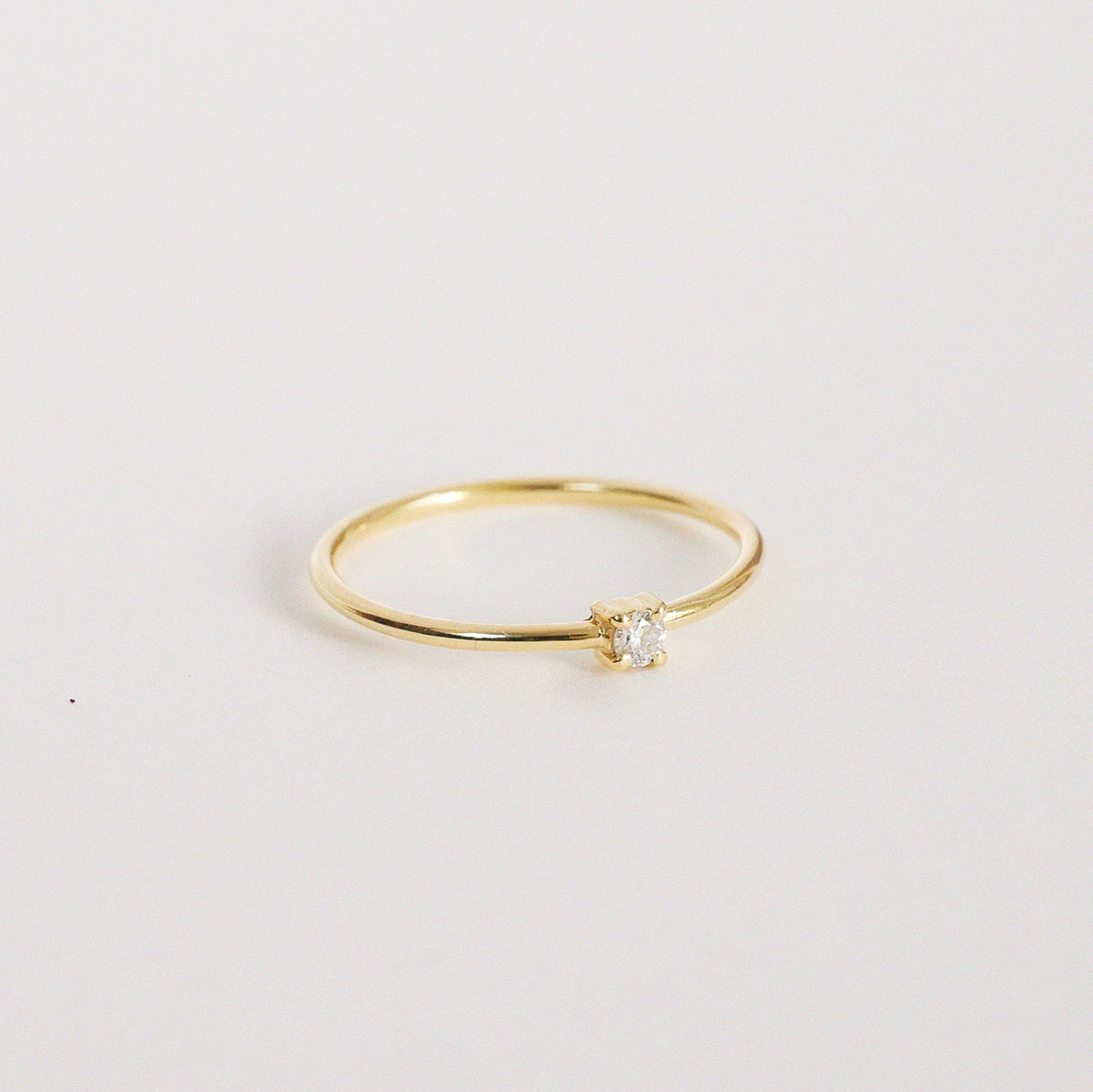 Anel solitário em ouro amarelo 18k com diamante em lapidação brilhante sobre fundo branco.