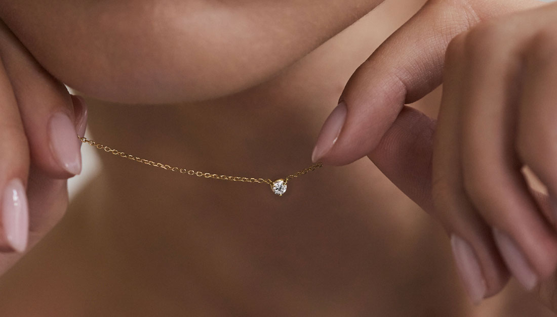 Modelo segurando colar solitário em ouro 18k com diamante brilhante.