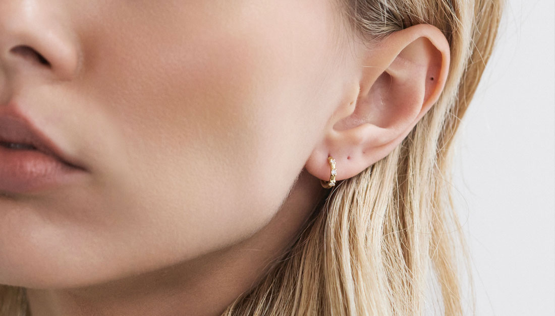 Modelo usando argola Trio Huggie em ouro 18k com três diamantes.