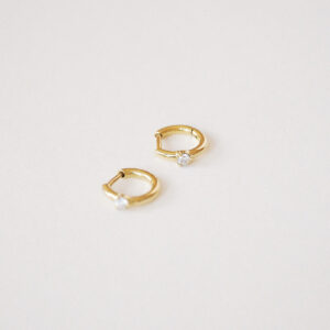 Par de Brincos Huggie Ponto em ouro amarelo 18k com diamantes sobre fundo off white.