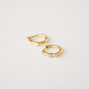 Brincos Trio Huggie em ouro 18k com três diamantes sobre fundo claro.