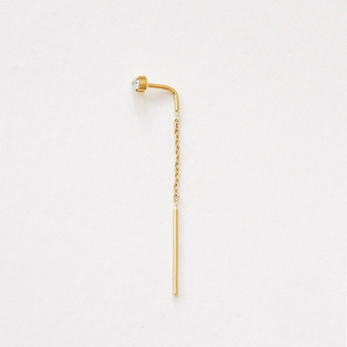 Brinco Linha (threader) em ouro amarelo 18k com diamante de 5 pontos e corrente delicada, fotografado sobre fundo off-white.