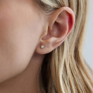 Close do brinco stud de diamante de 10 pontos em ouro 18k na orelha.